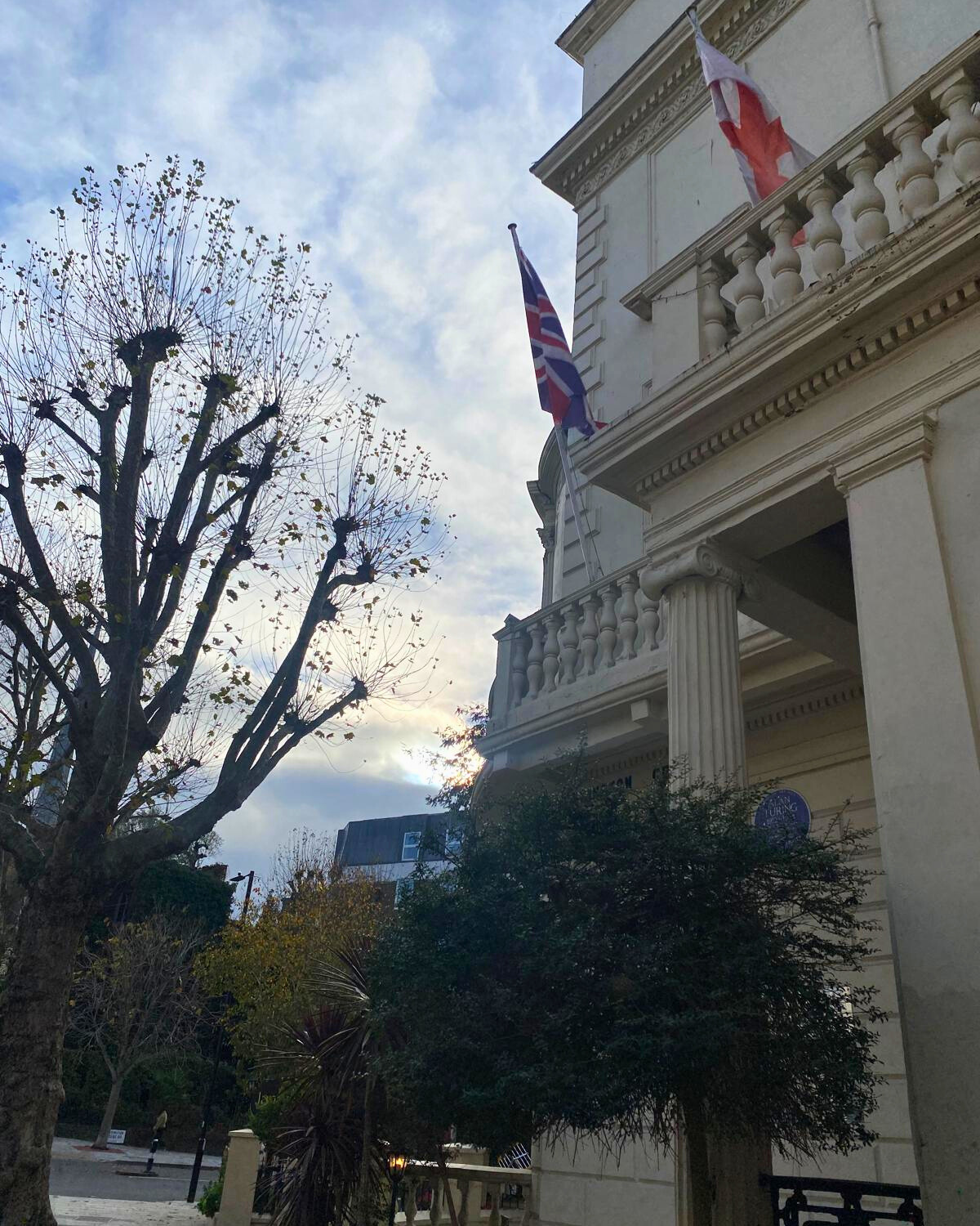 Street view of the building with flags, columns and trees in the foreground.