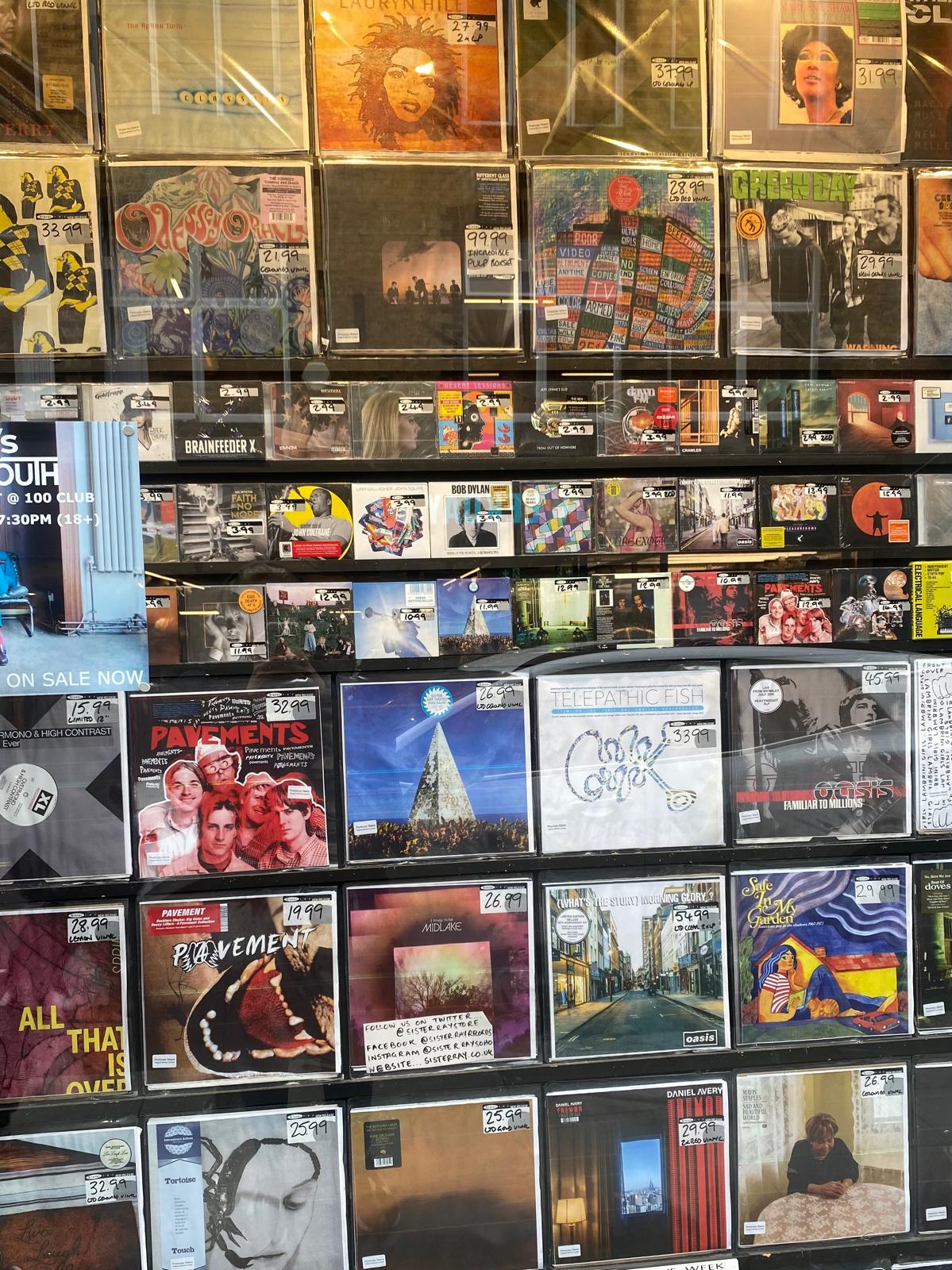 Storefront window display filled with rows of vinyl records from various artists.