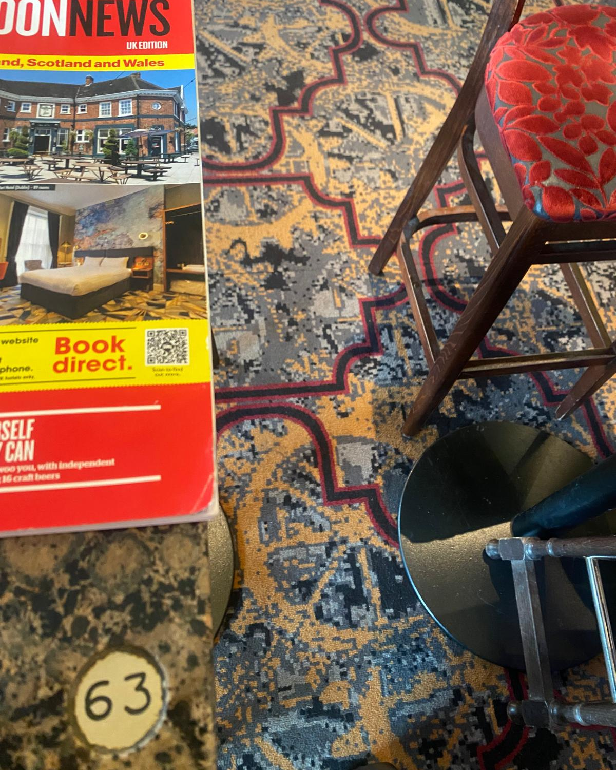 Close-up of a pub table with a magazine, chair leg and the pub’s distinctive patterned carpet visible.
